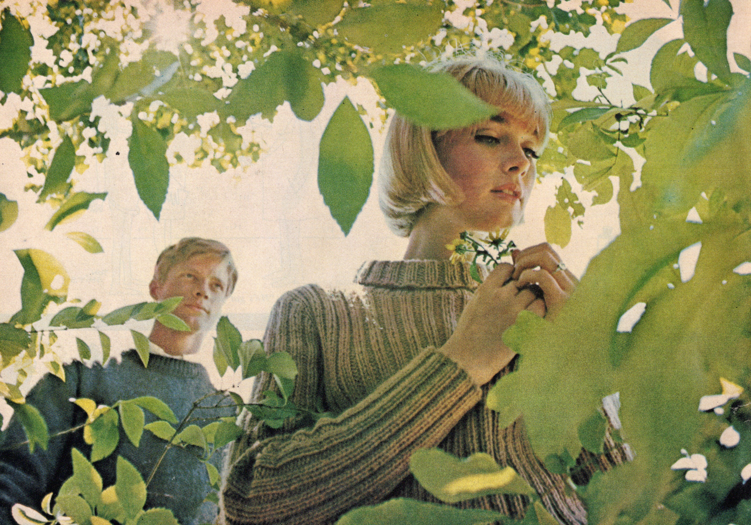 Two people standing among green foliage and flowers